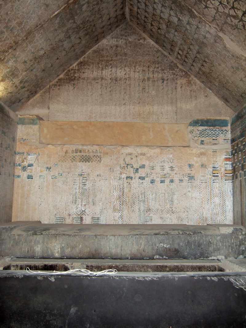 Chambre funéraire de la pyramide d’Ounas, colonnes d’hiéroglyphes au mur, plafond étoilé et sarcophage.